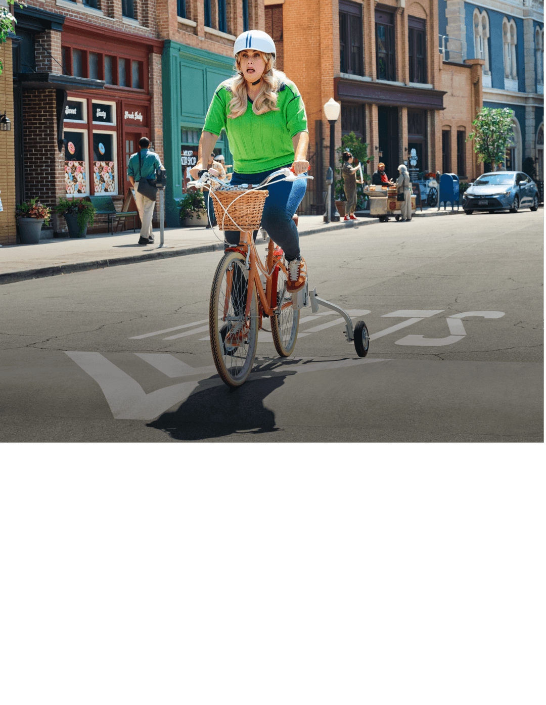 Woman riding a bike with training wheels down a city street