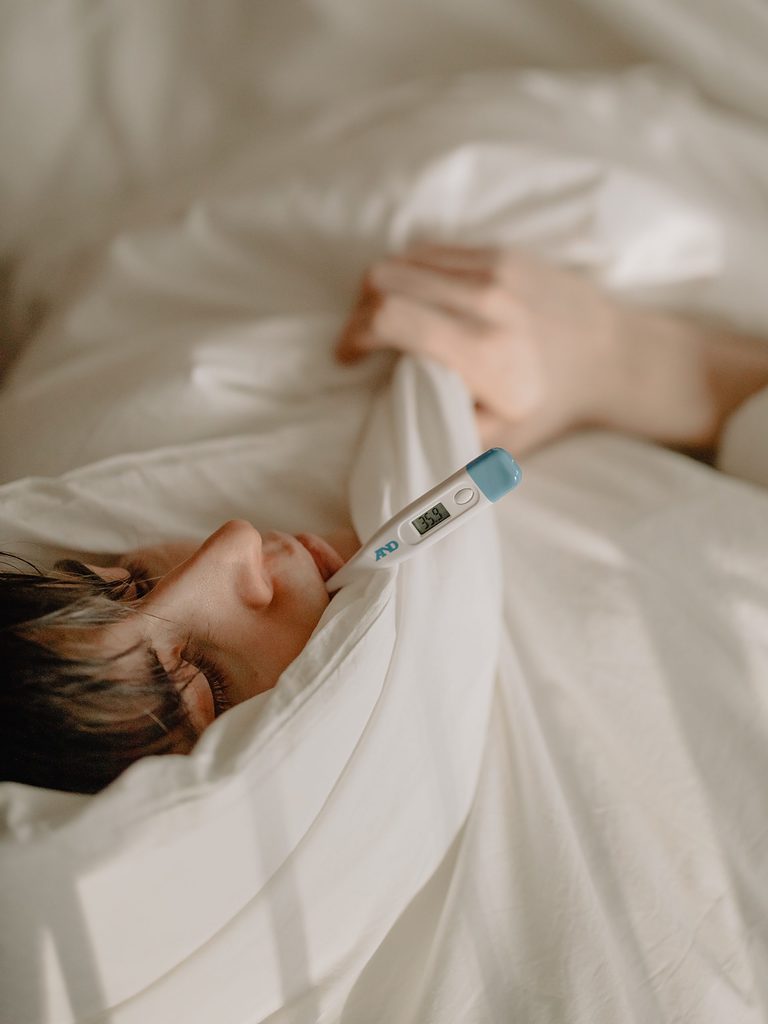 Sick person lying in bed with a thermometer