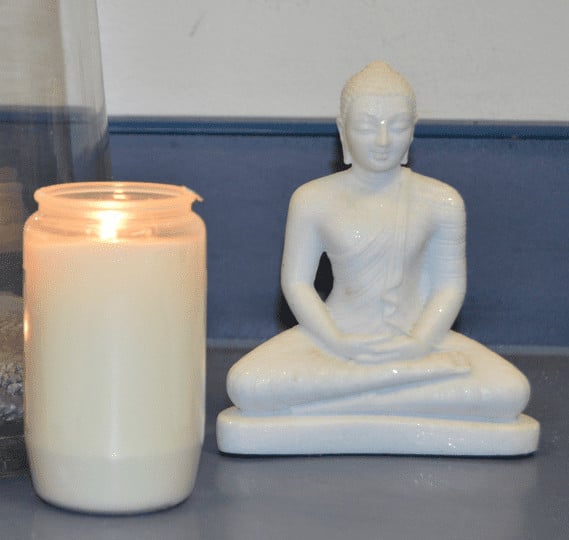 Kleine weiße Buddhafigur neben einer Kerze